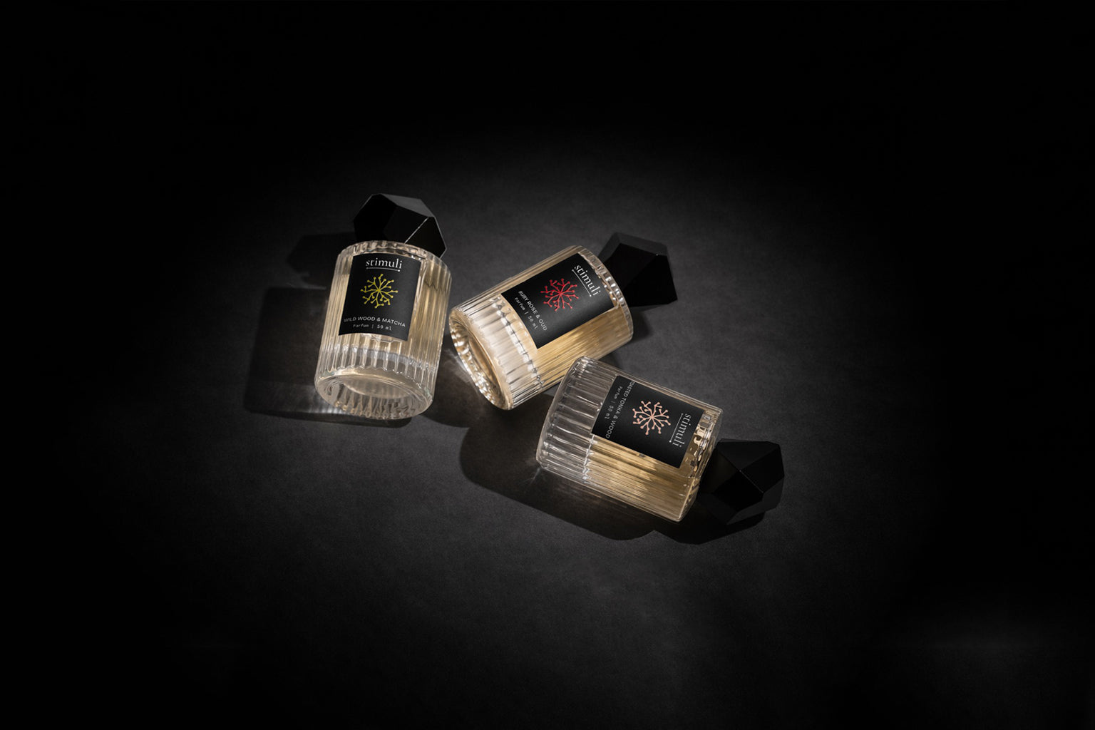 Three Stimuli parfum bottles with labels on a dark background